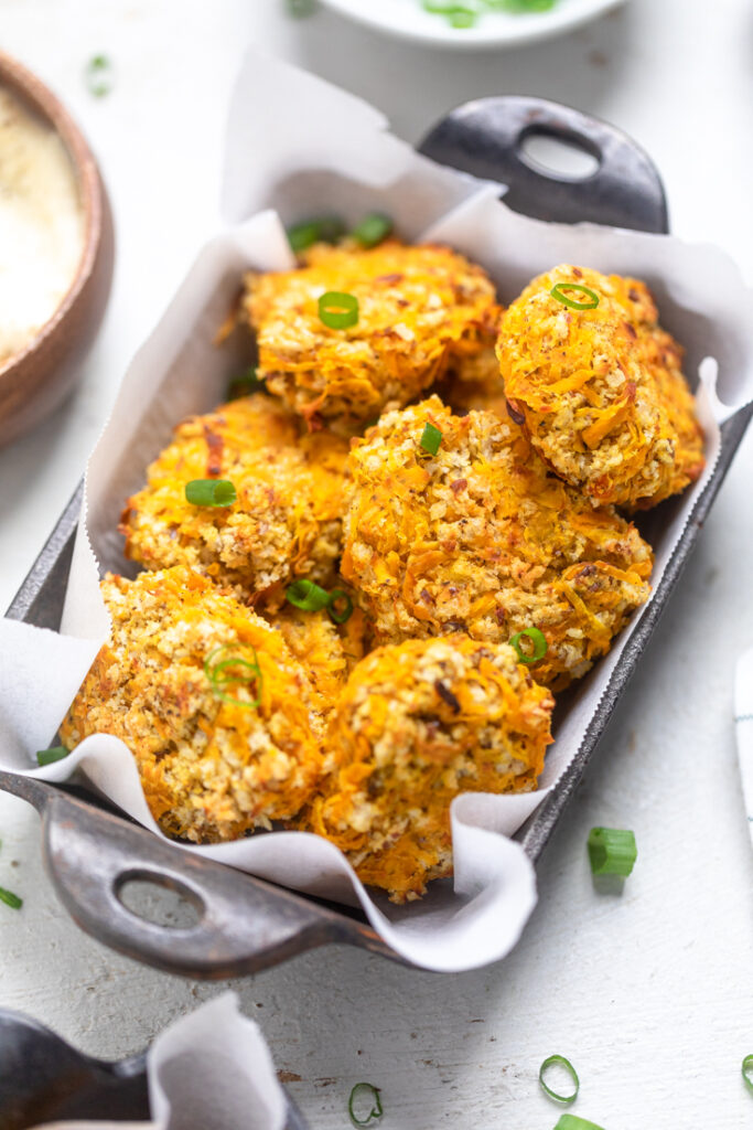 A black serving tray of vegan butternut squash nuggets topped with green onions.