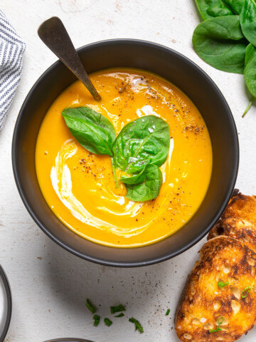 A bowl of Vegan Carrot Ginger Soup with fresh basil leaves.