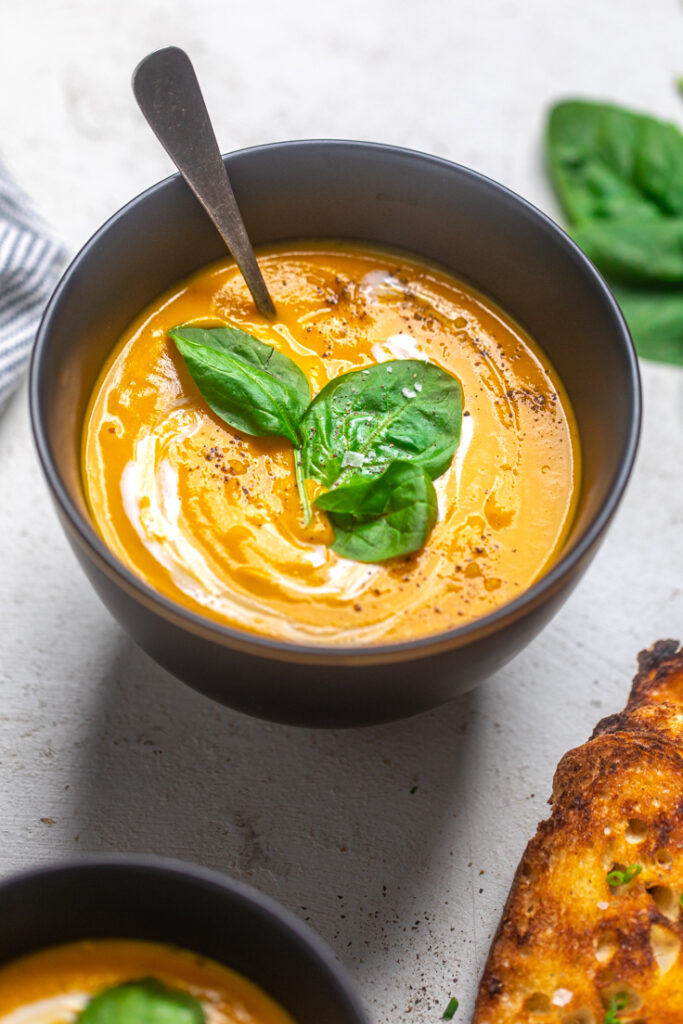 A bowl of Vegan Carrot Ginger Soup with cracked black pepper, basil and cream.