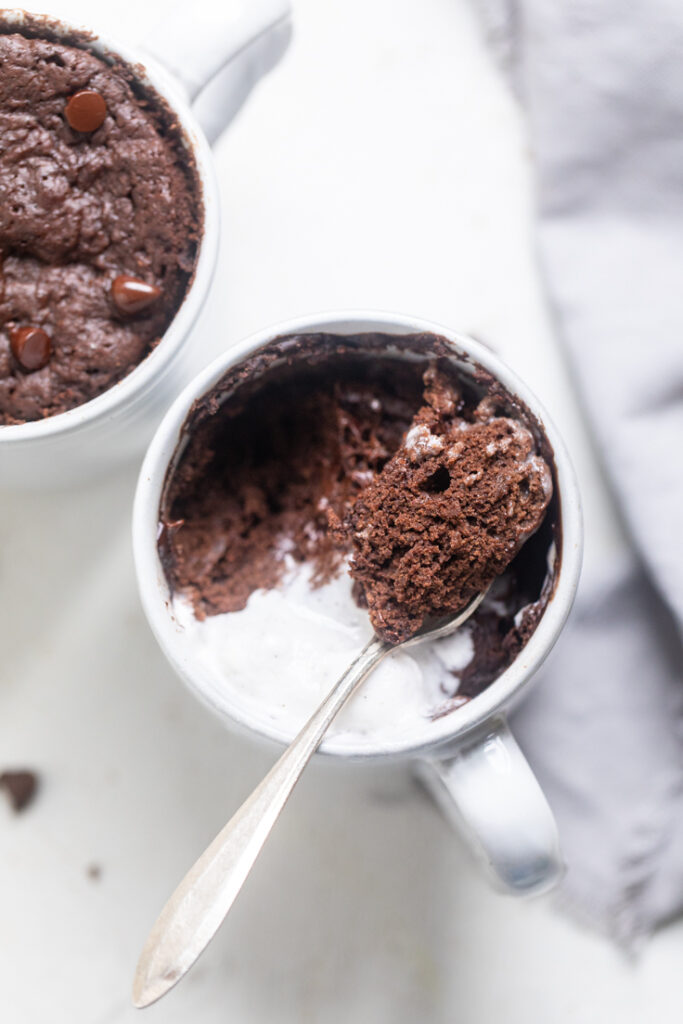 A vegan chocolate mug cake with whip and a spoon laying on top with cake.
