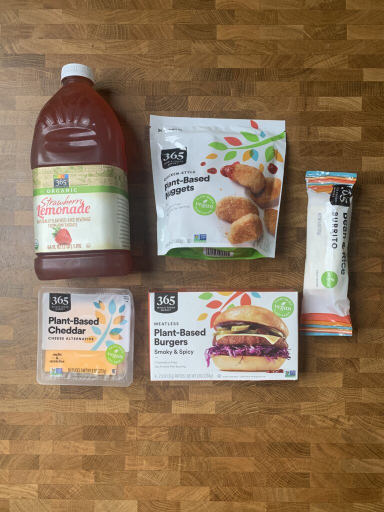 An assortment of 365 vegan main dish product packages and a juice bottle on a table.