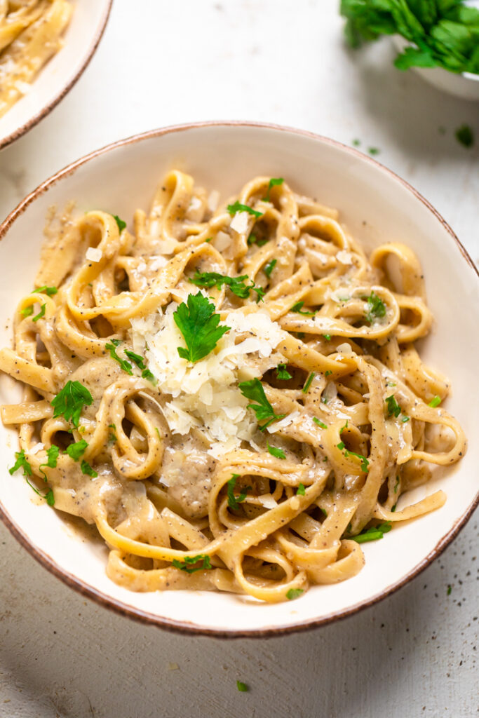 A white bowl of vegan one pot creamy garlic parmesan pasta topped with fresh parsley.