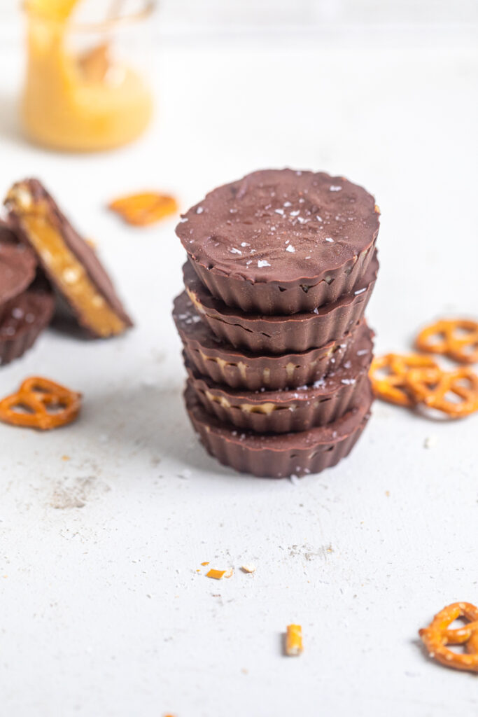 Vegan peanut butter pretzel cups stacked on a white table with additional pretzels.