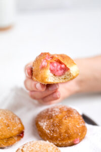 A hand holding a vegan strawberry cream filled donuts with a bite missing.