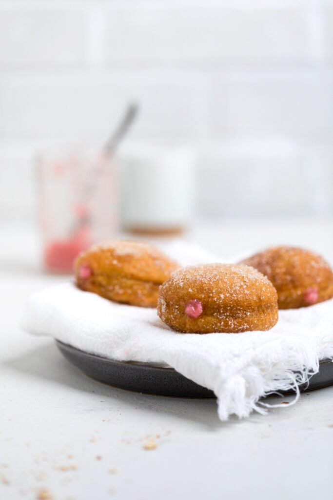 A batch of vegan strawberry cream filled donuts on a towel lined plate.
