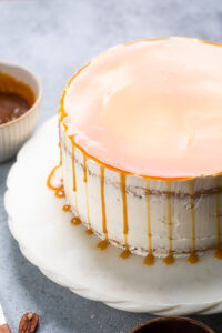 Vegan Caramel Cake on a white cake stand with caramel poured over the top.