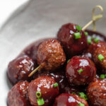Two vegan grape jelly meatballs skewered atop more meatballs.