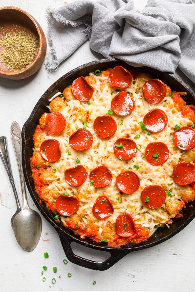 A black cast iron skillet of Vegan Pizza tater tot casserole with pepperoni.