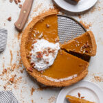 A cooked Vegan Sweet Potato Pie with a slice removed and vegan whipped topping.