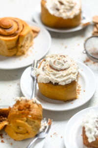 One frosted Vegan Sweet Potato Pie Cinnamon Roll on a white plate.