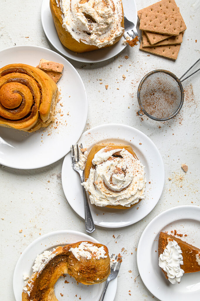 Two Vegan Sweet Potato Pie Cinnamon Rolls on plates, one frosted and one not.