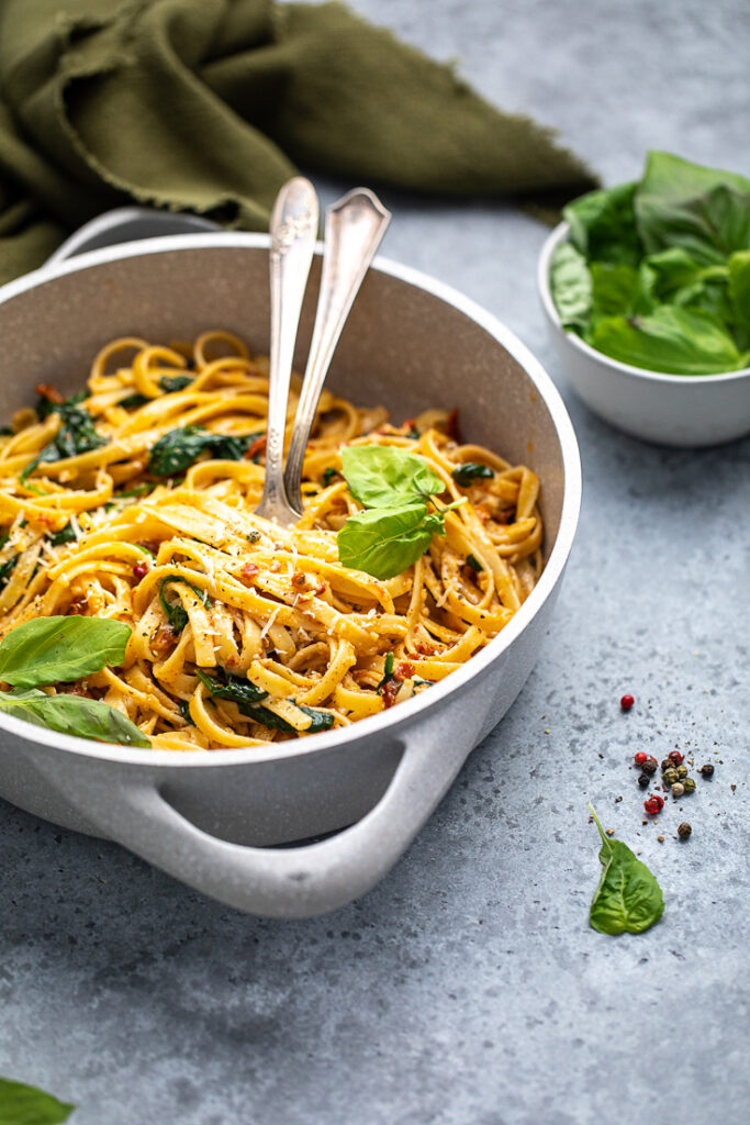 A pot of cooked Easy Vegan Spinach and Sundried Tomato Pasta topped with fresh basil. 