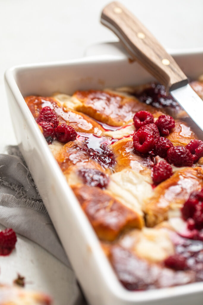 A white dish of Raspberry Vegan Crescent French Toast Casserole with syrup poured over.
