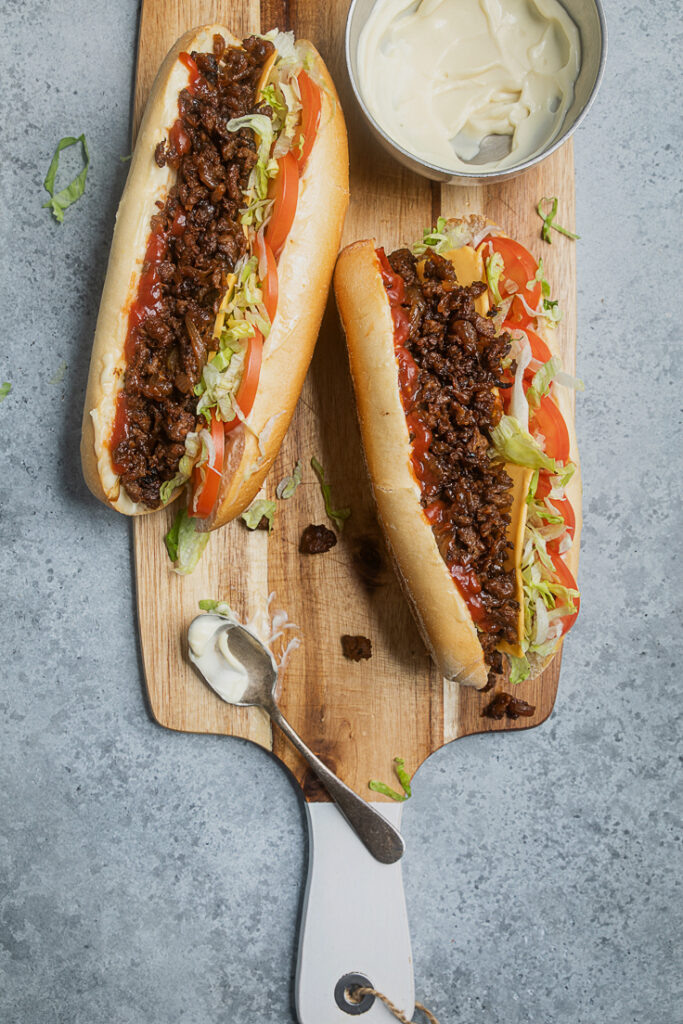 Two vegan chopped cheese sandwiches on a wooden board.