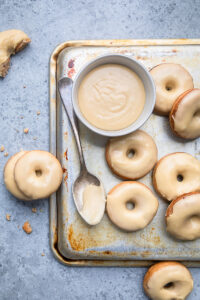 Vegan Maple Donuts on a tray with a spoon and bowl of glaze.