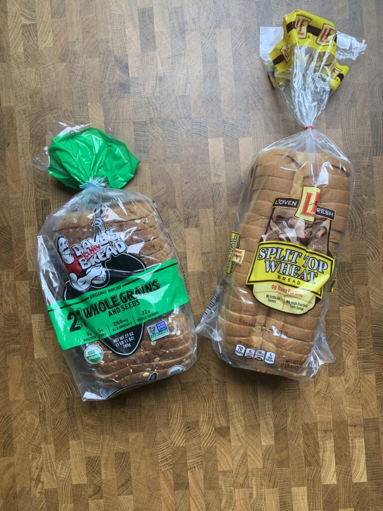 A loaf of Dave\'s Bread and a Loaf of L\'oven Fresh split top wheat bread.
