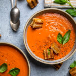 A bowl of Vegan Tomato Soup with fresh basil and cracked black pepper with grilled cheese.