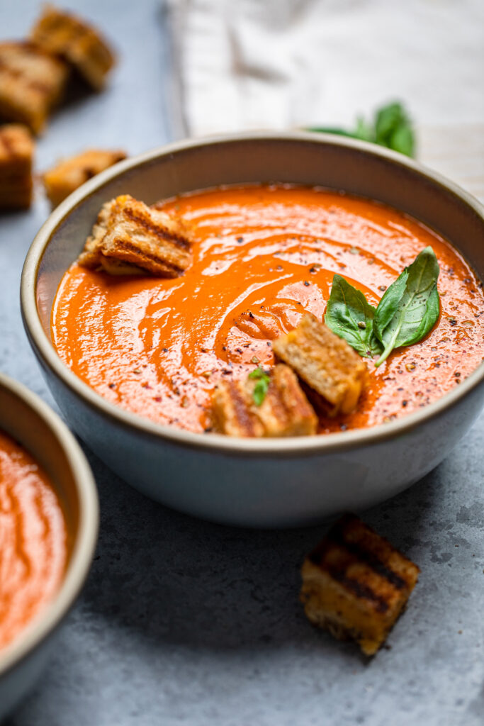 A gray serving bowl of Vegan Tomato Soup topped with fresh basil.