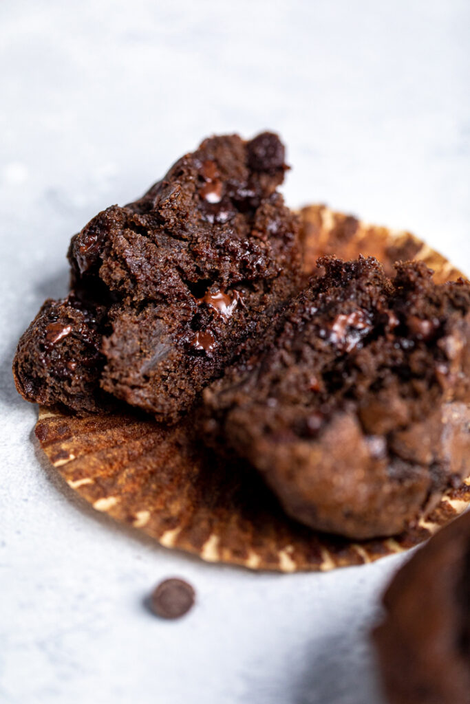 A vegan double chocolate muffin halved laying on a muffin wrapper.