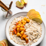 Vegan apple cinnamon oatmeal in a bowl with cooked diced apples and apple slices on top.