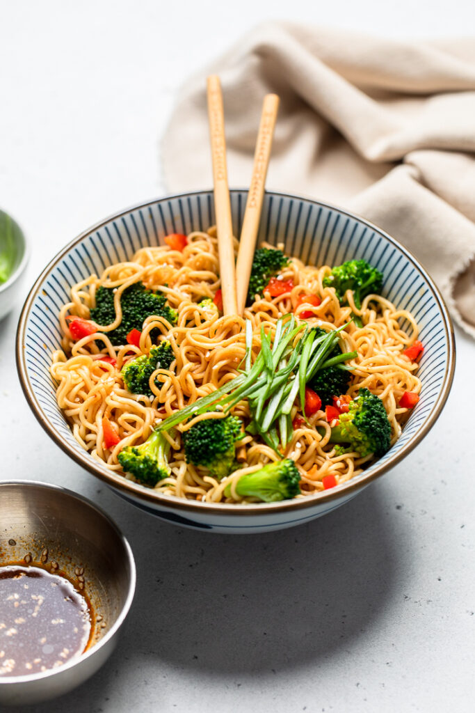 A striped bowl of easy vegan broccoli and pepper ramen noodles topped with green onions.
