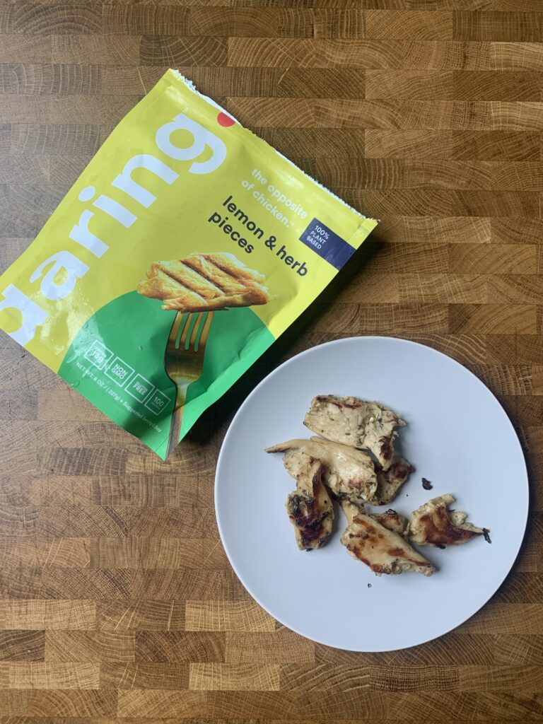 Daring lemon & herb vegan chicken package next to a plate of cooked pieces. 