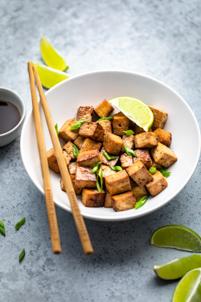 A bowl of vegan garlic soy lime tofu with lime wedges.