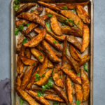 A tray of vegan seasoned potato wedges cooked and topped with parsley.