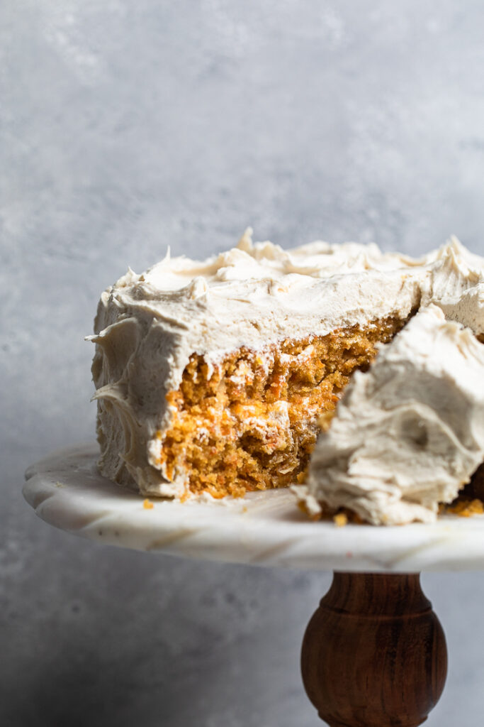 A white cake stand with double layered vegan coconut carrot cake.