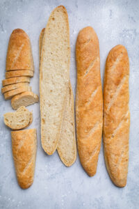 Four Vegan Baguettes on a table,  two whole, and two slices differently.