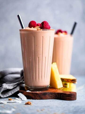Two clear glasses of Vegan Mango pina colada smoothie with raspberries on top.