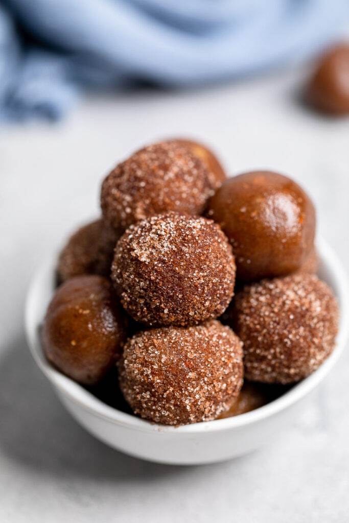 A bunch of vegan snickerdoodle energy bites stacked on top of each other in white bowl.
