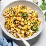 A speckled bowl of copycat chipotle roasted corn salsa with a silver spoon on the side.