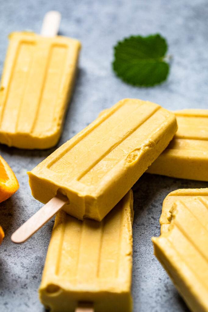 A vegan orange creamsicle popsicle with a wooden stick. 