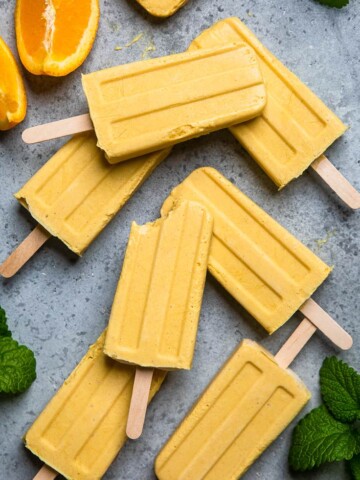 A batch of vegan orange creamsicle popsicles, one with a bite out.