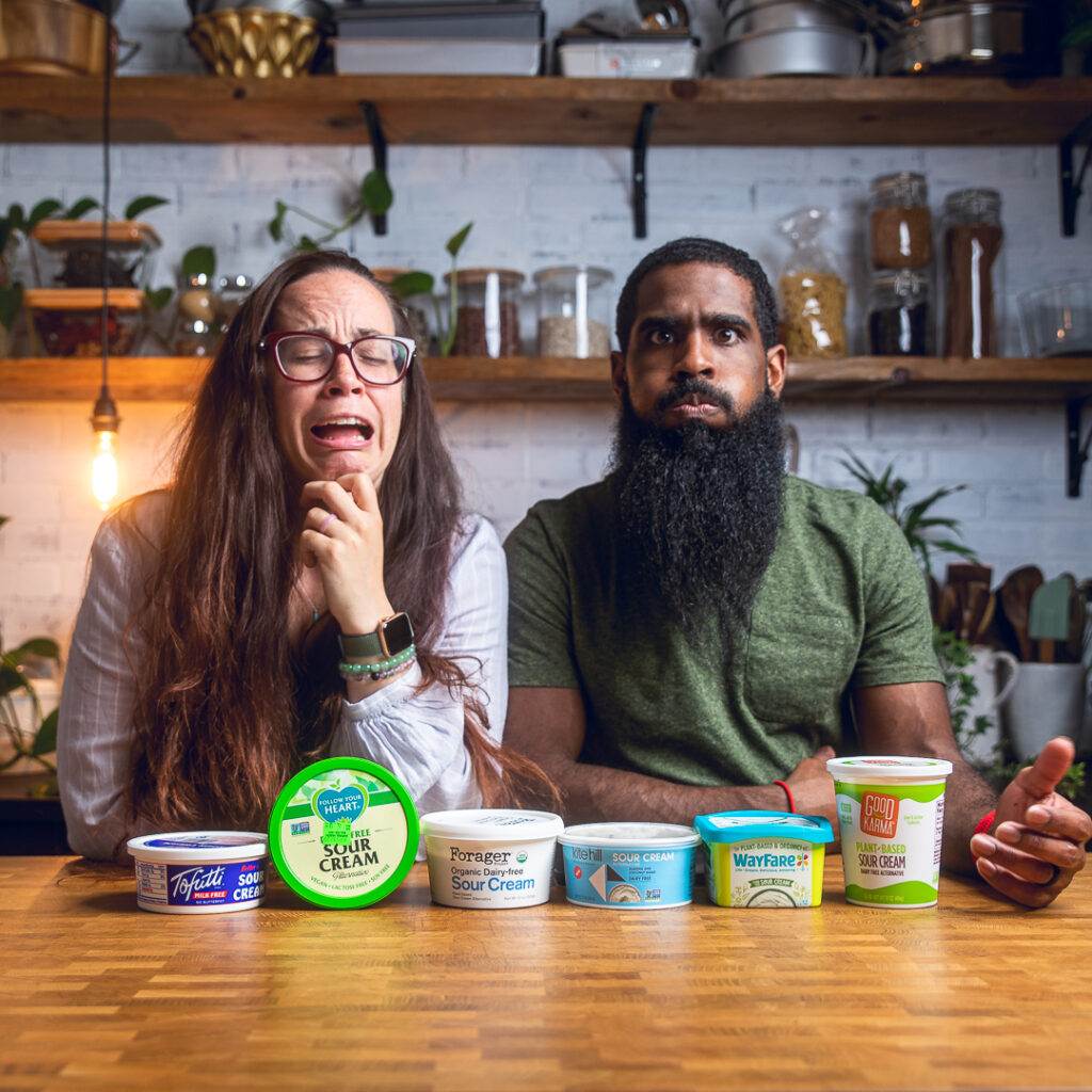 A couple making funny faces posing behind an table of vegan sour cream products.