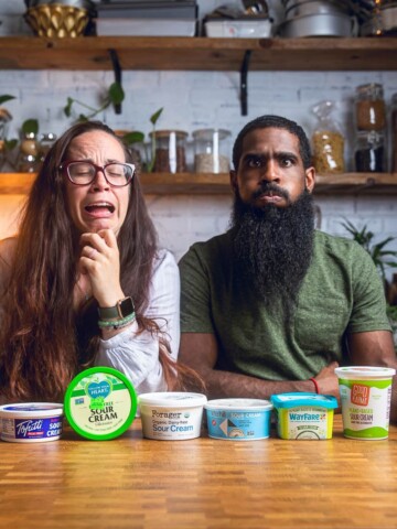 A couple posing behind an assortment of vegan sour cream product containers making funny faces.