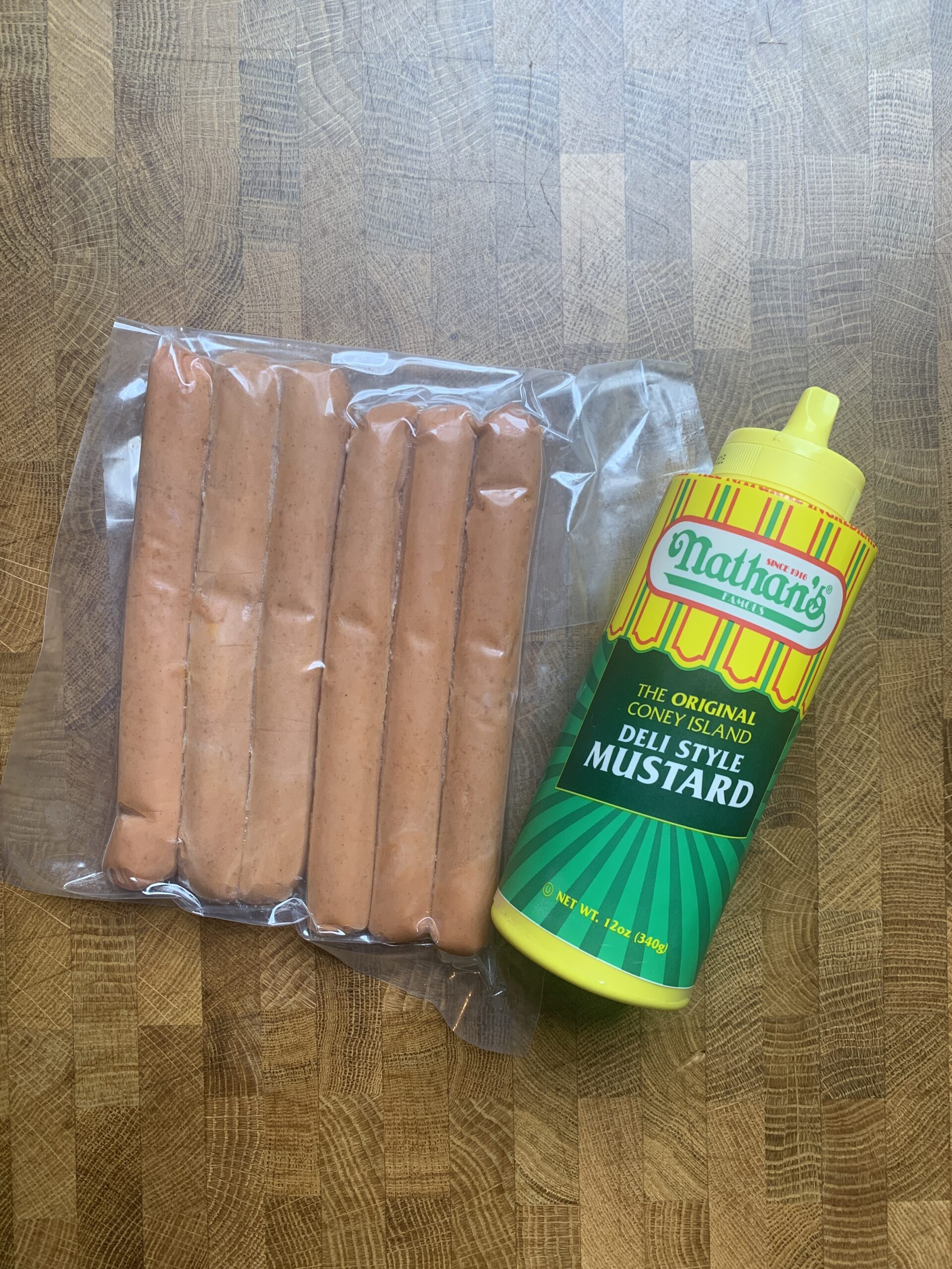 A pack of uncooked vegan hotdogs and a bottle of Nathan\'s deli style mustard.