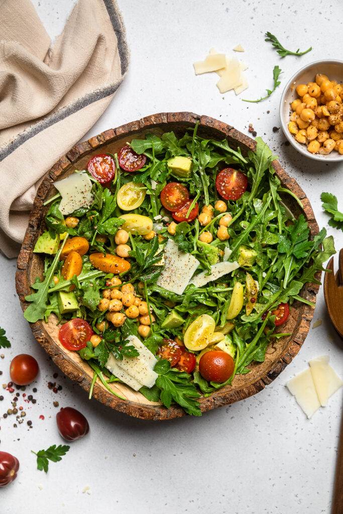 A large serving dish of vegan arugula salad with fresh vegetables and chickpeas.