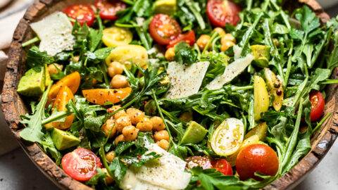 Vegan arugula salad with chickpeas, avocado and cherry tomatoes inside a wooden bowl.