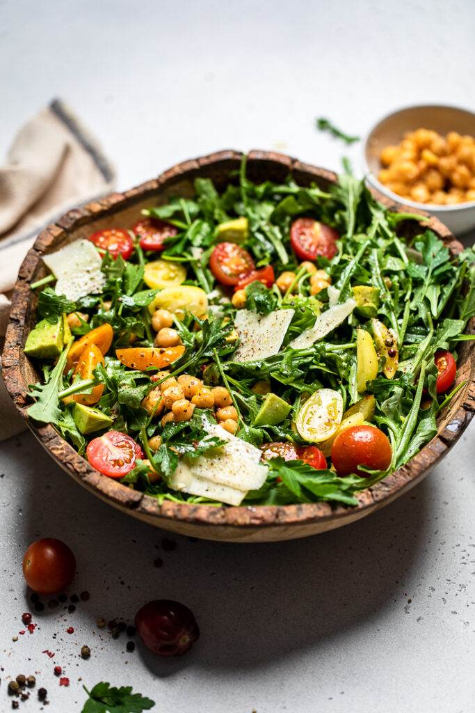 Vegan arugula salad in a bowl with chickpeas, avocado and cherry tomatoes.