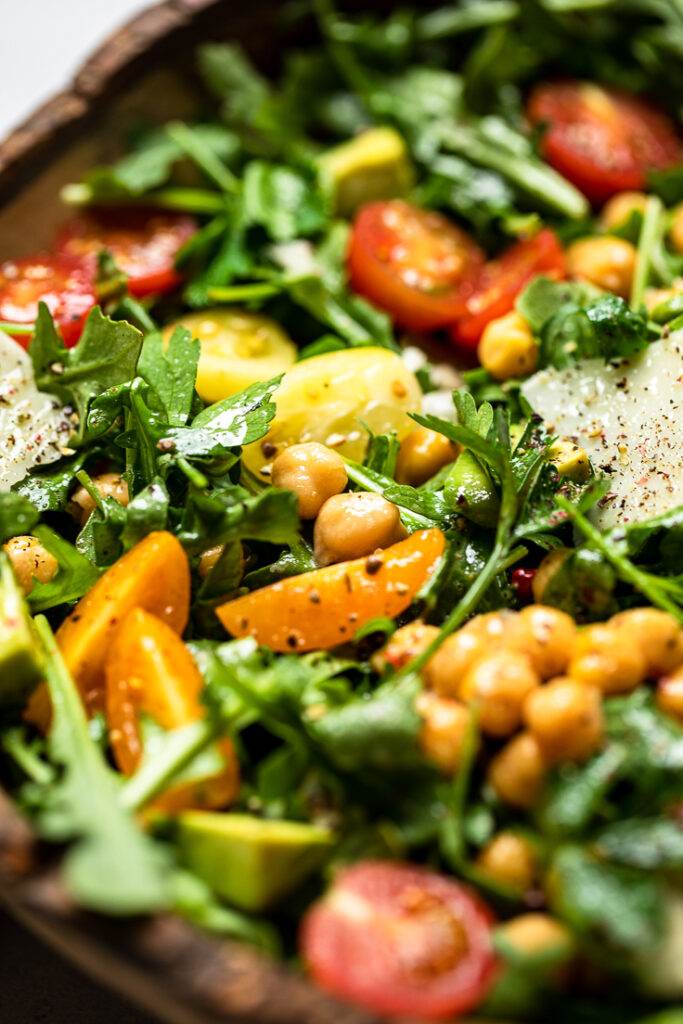 A serving of vegan arugula salad with chickpeas, avocado and cherry tomatoes with light dressing.