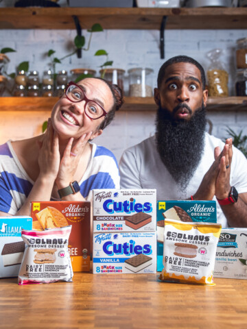 A couple making silly faces posing behind a table of vegan ice cream sandwiches packages.