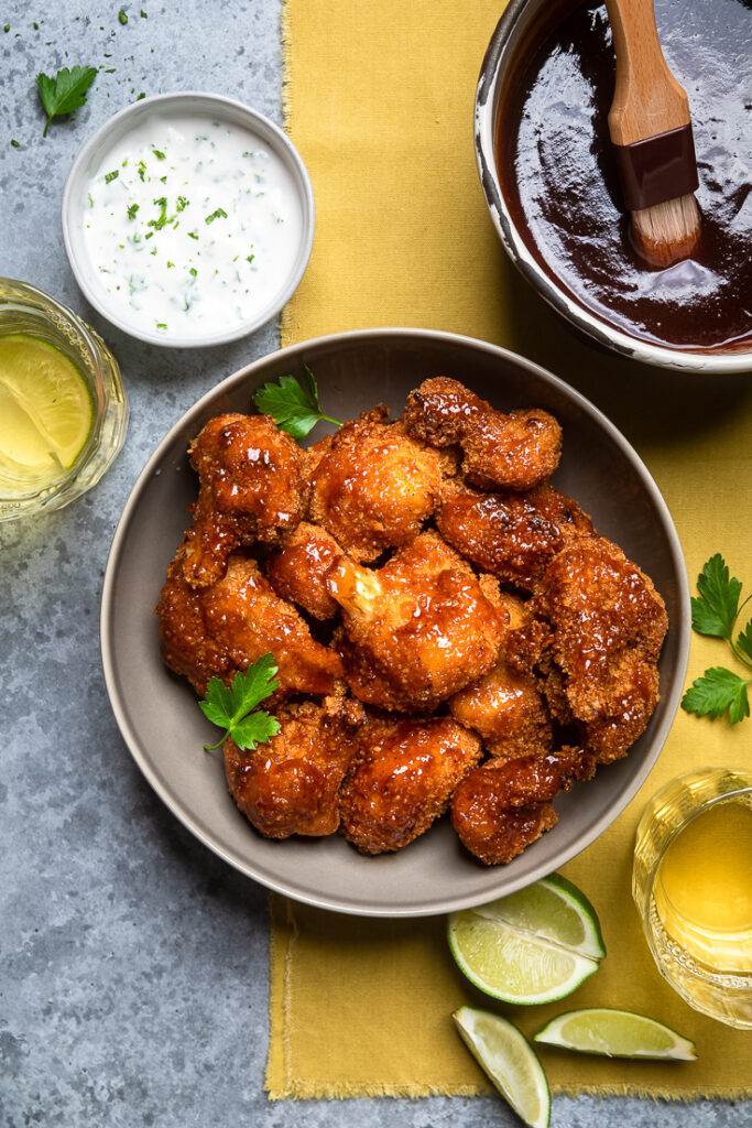 A serving dish of Vegan BBQ Cauliflower Wings with extra sauce and ranch on the side.
