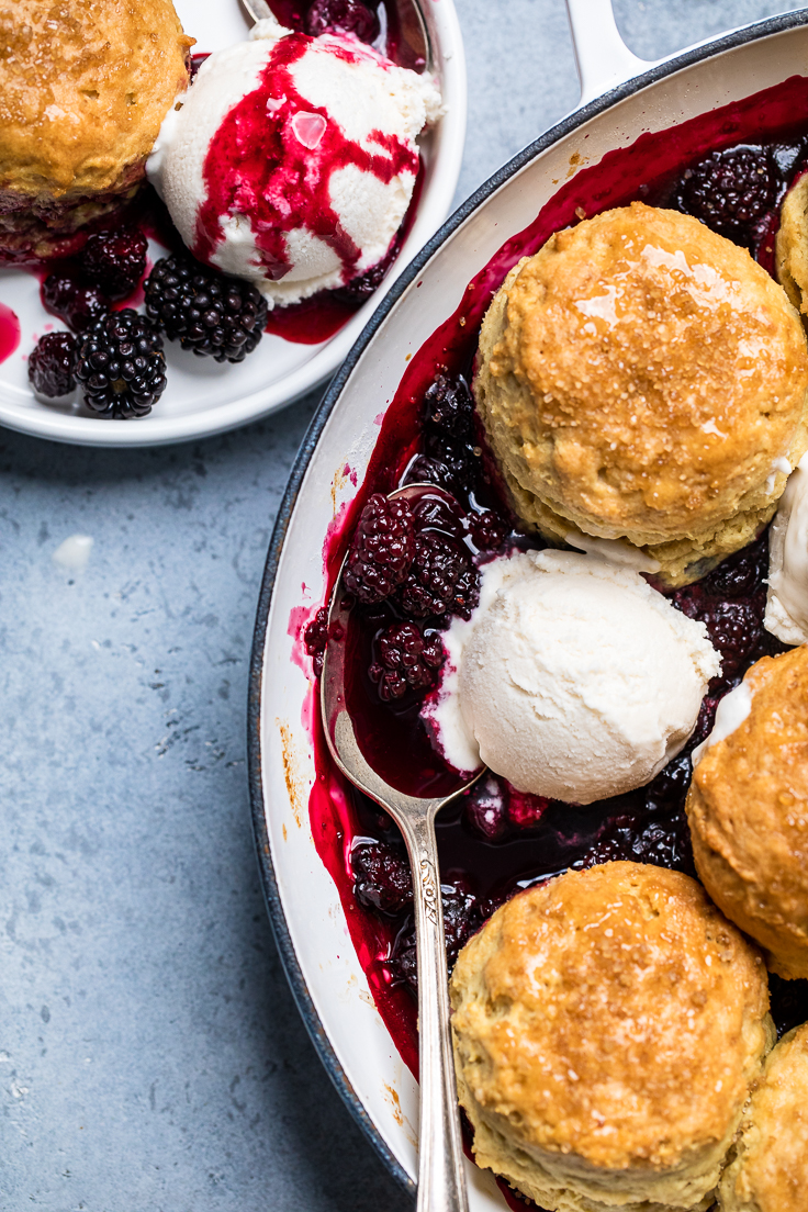 A serving dish of vegan blackberry cobbler topped with biscuits and vegan ice cream.
