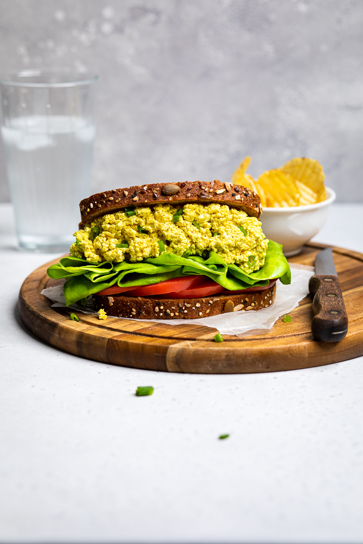 Easy vegan egg salad sandwich with lettuce and tomato on a wooden cutting board.
