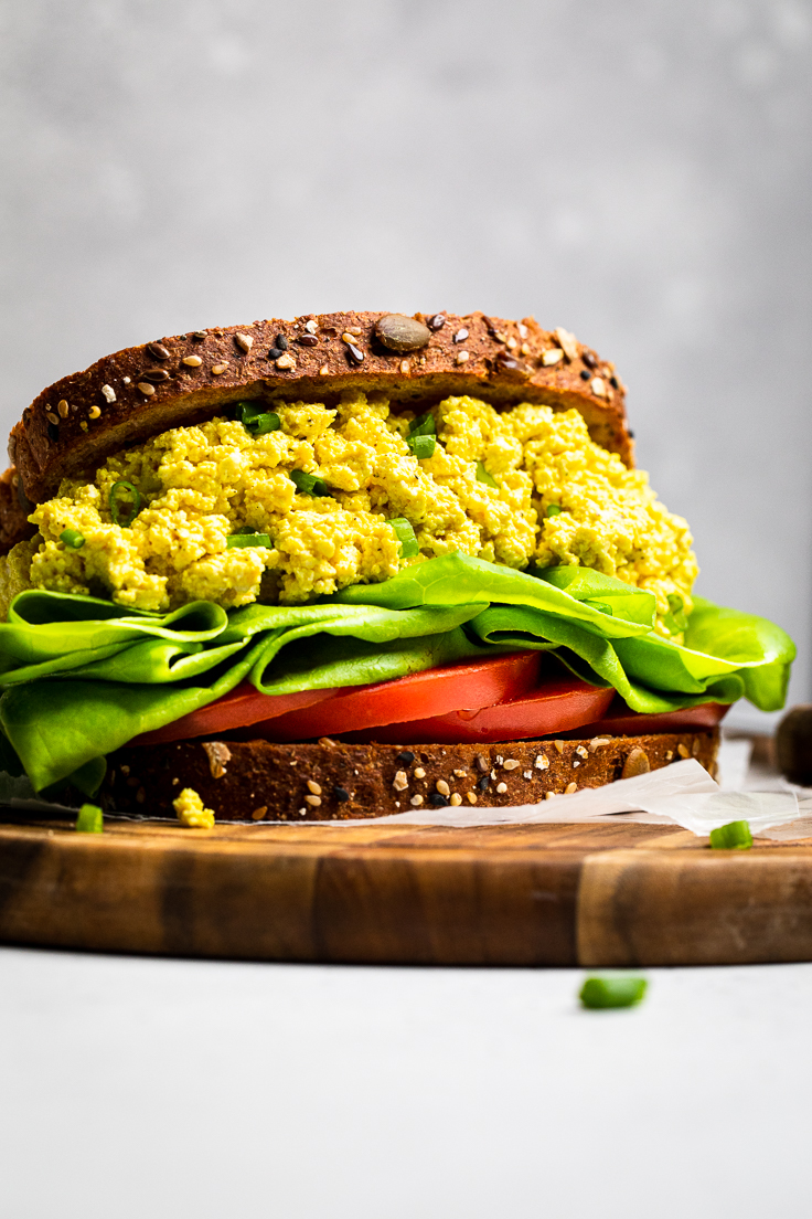 Easy vegan egg salad piled high on two slices of seeded bread with lettuce and tomato. 