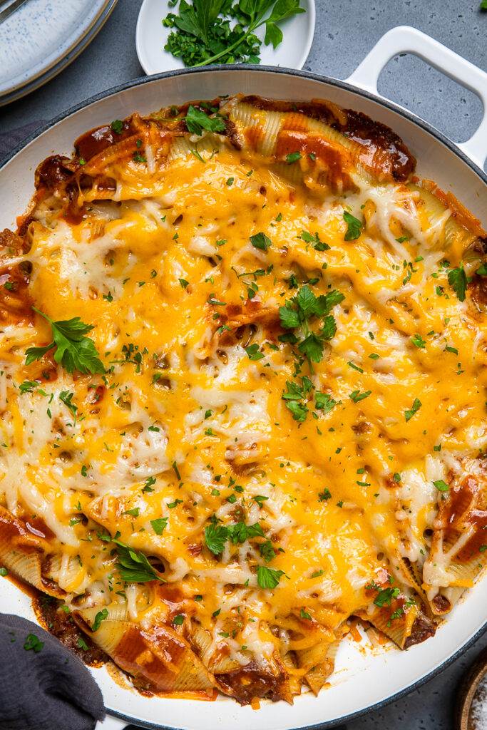A skillet of vegan stuffed shells filled with enchilada filling and topped with vegan cheese.