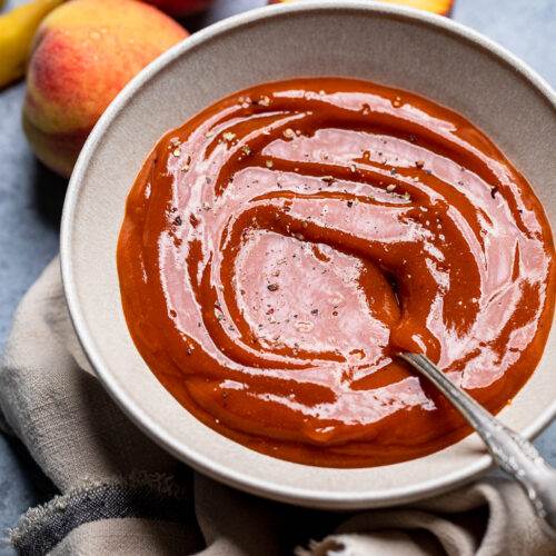 Vegan Peach BBQ sauce with a spoon and topped with fresh black pepper.