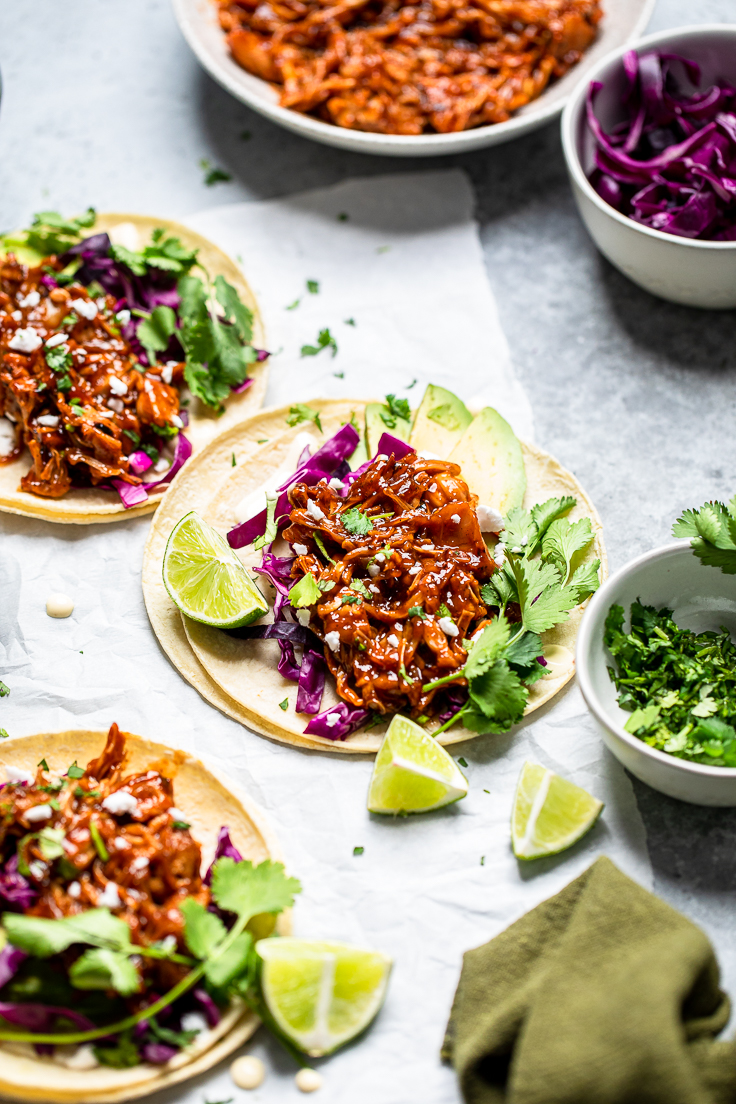 Three grilled vegan jackfruit tacos laying flat on a table with fresh cilantro and limes.